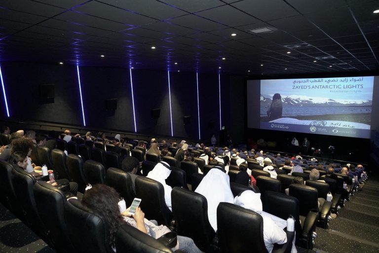 People sitting in a theatre and watching a movie on screen