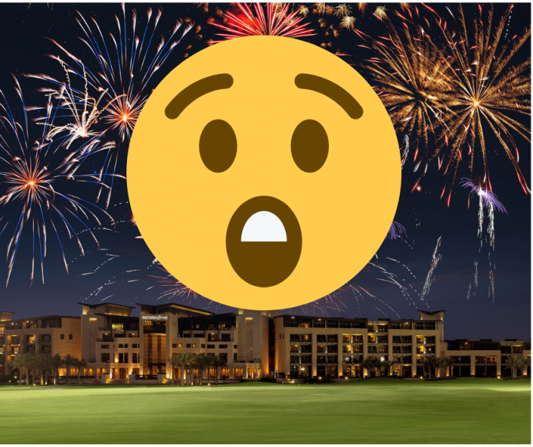 A surprised emoji with Firworks in blue sky over green grass and some lit building in the background