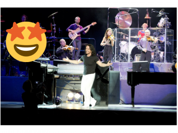 A Man Standing on a performace stage with his open arms with a muscial orchestra arranagement in the background