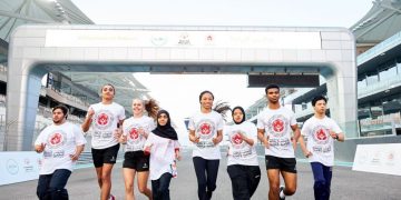 People running on a track wearing a common teshirt with writings on it