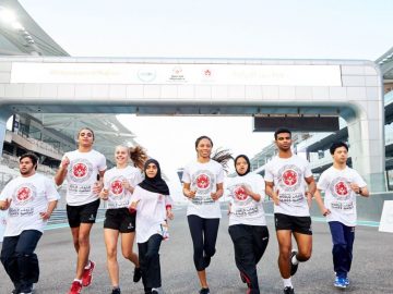 People running on a track wearing a common teshirt with writings on it