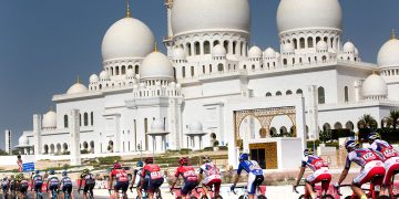 Cyclists riding in colorful jerseys with a white marble mosque in the background