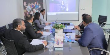 Group of people sitting around a table and looking at a projection on a screen