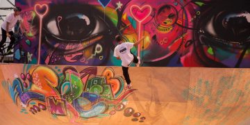 A skateboarder in the air on a wooden ramp with colorful graffiti in the foreground