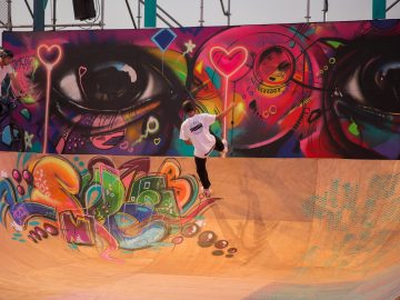 A skateboarder in the air on a wooden ramp with colorful graffiti in the foreground
