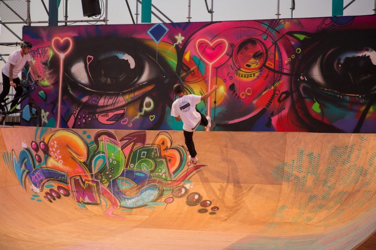 A skateboarder in the air on a wooden ramp with colorful graffiti in the foreground