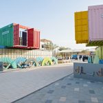 Ship cargo containers painted in red, green, yellow and pink stacked on each other with a cut open door on them