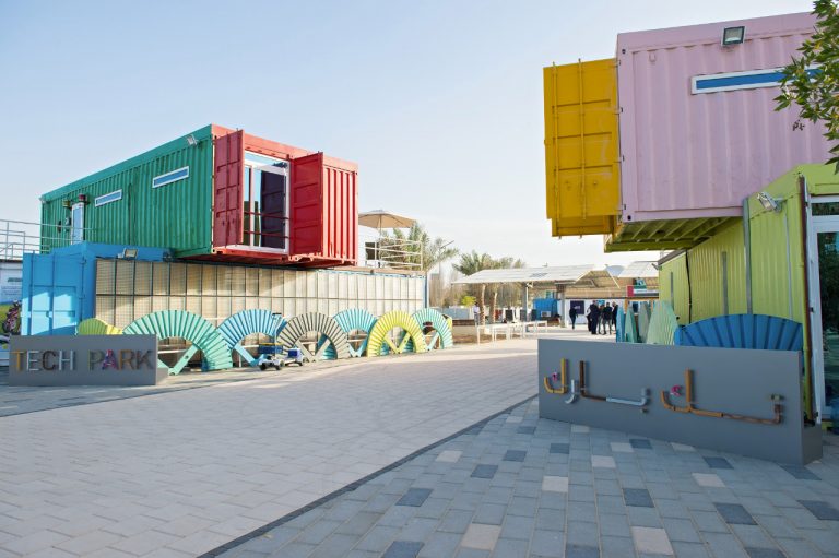 Ship cargo containers painted in red, green, yellow and pink stacked on each other with a cut open door on them