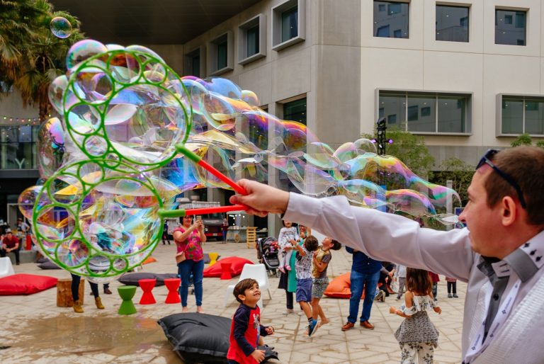 Hand shot of a bubble maker making bubbles with kids looking at the bubbles in the background