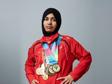 An athelete in red jacket and black head scarf posing with meadls around her neck
